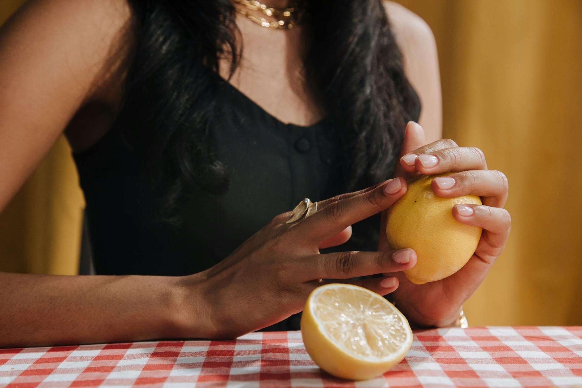 Hand holding a lemon clitoral vibrator against a minimalist purple backdrop.