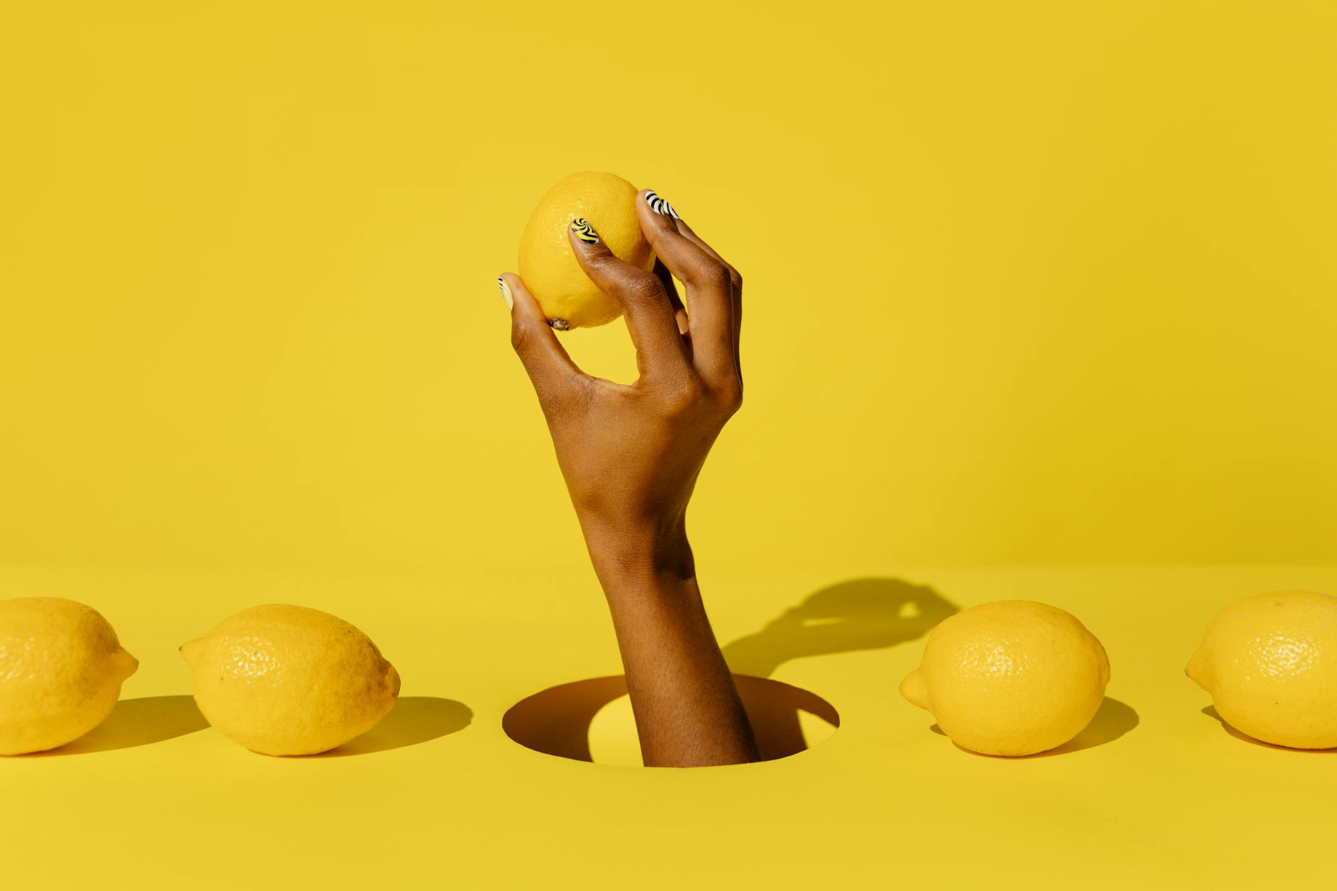 A hand holding a fresh lemon against a vivid yellow background, symbolizing renewal and vitality