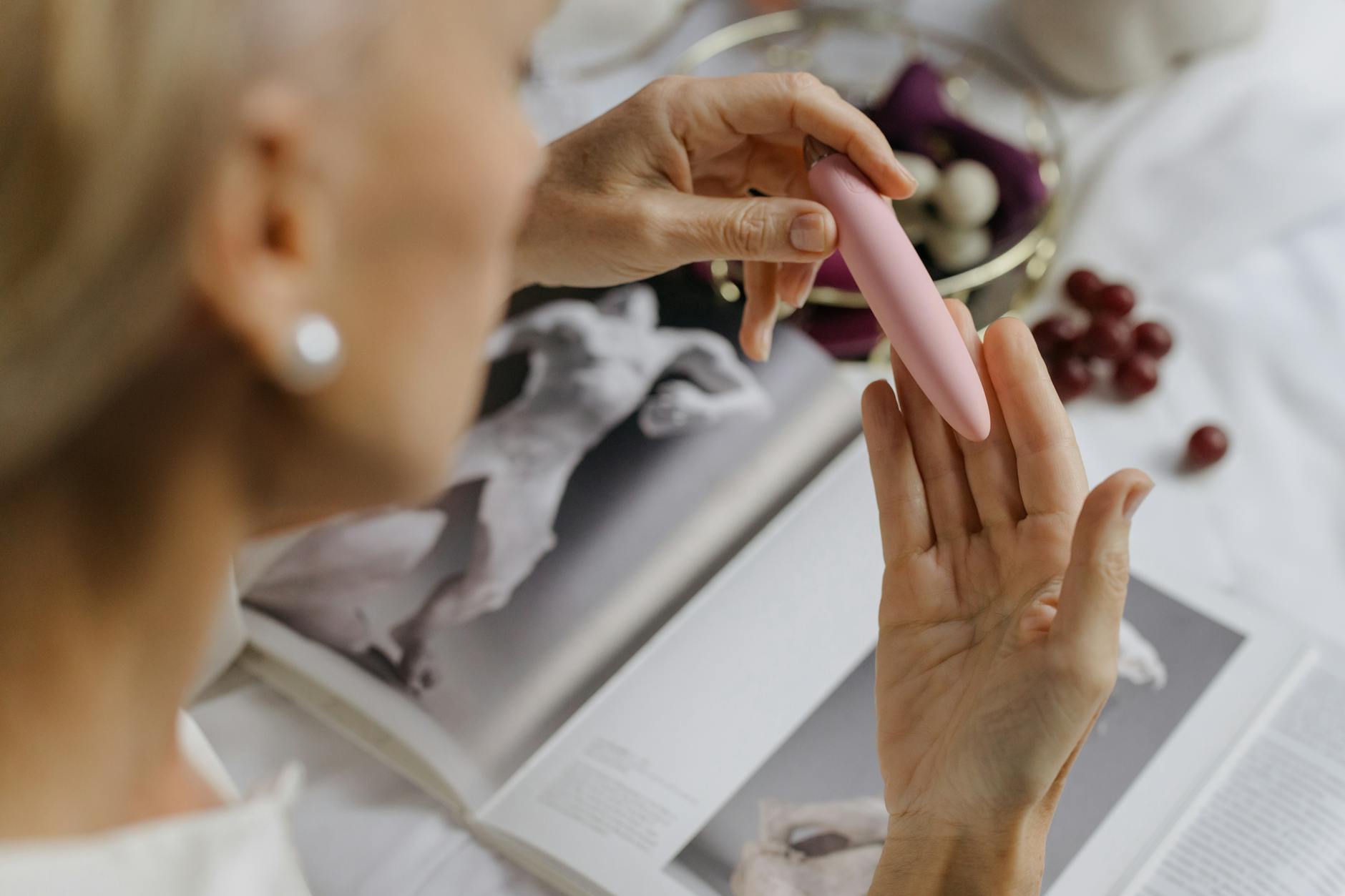 Close-up of a woman holding a pink vibrator with art books in background