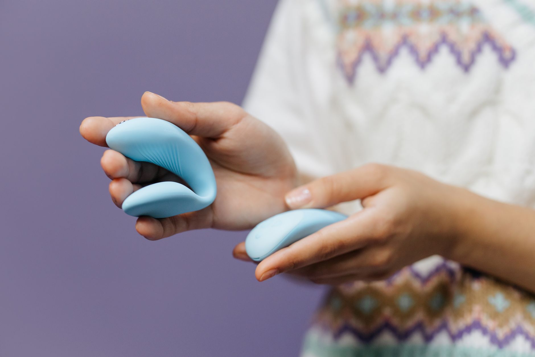 Hände halten einen schlanken blauen Vibrator gegen zartem lila Hintergrund