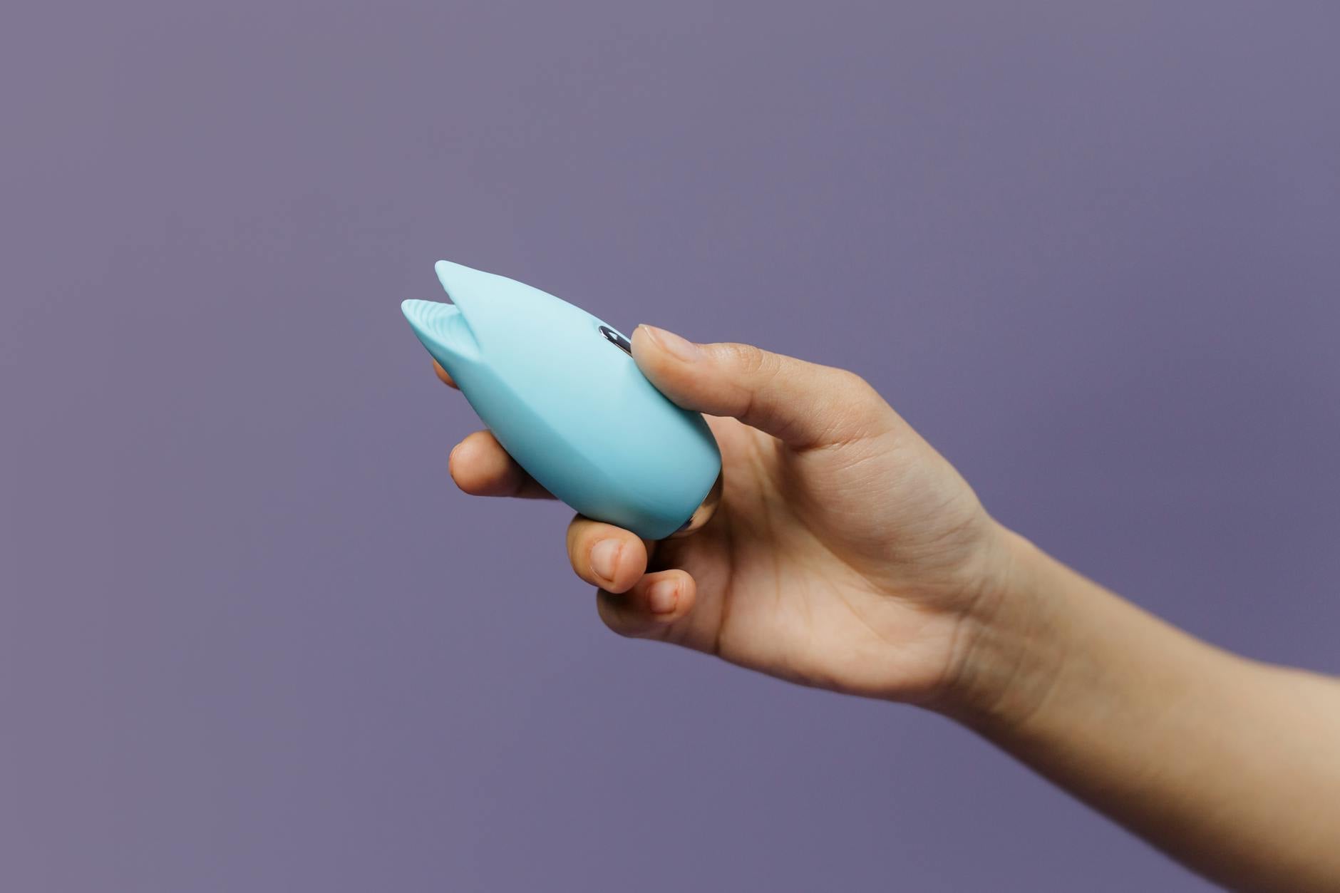 A person holding a sleek blue lemon vibrator against a purple background