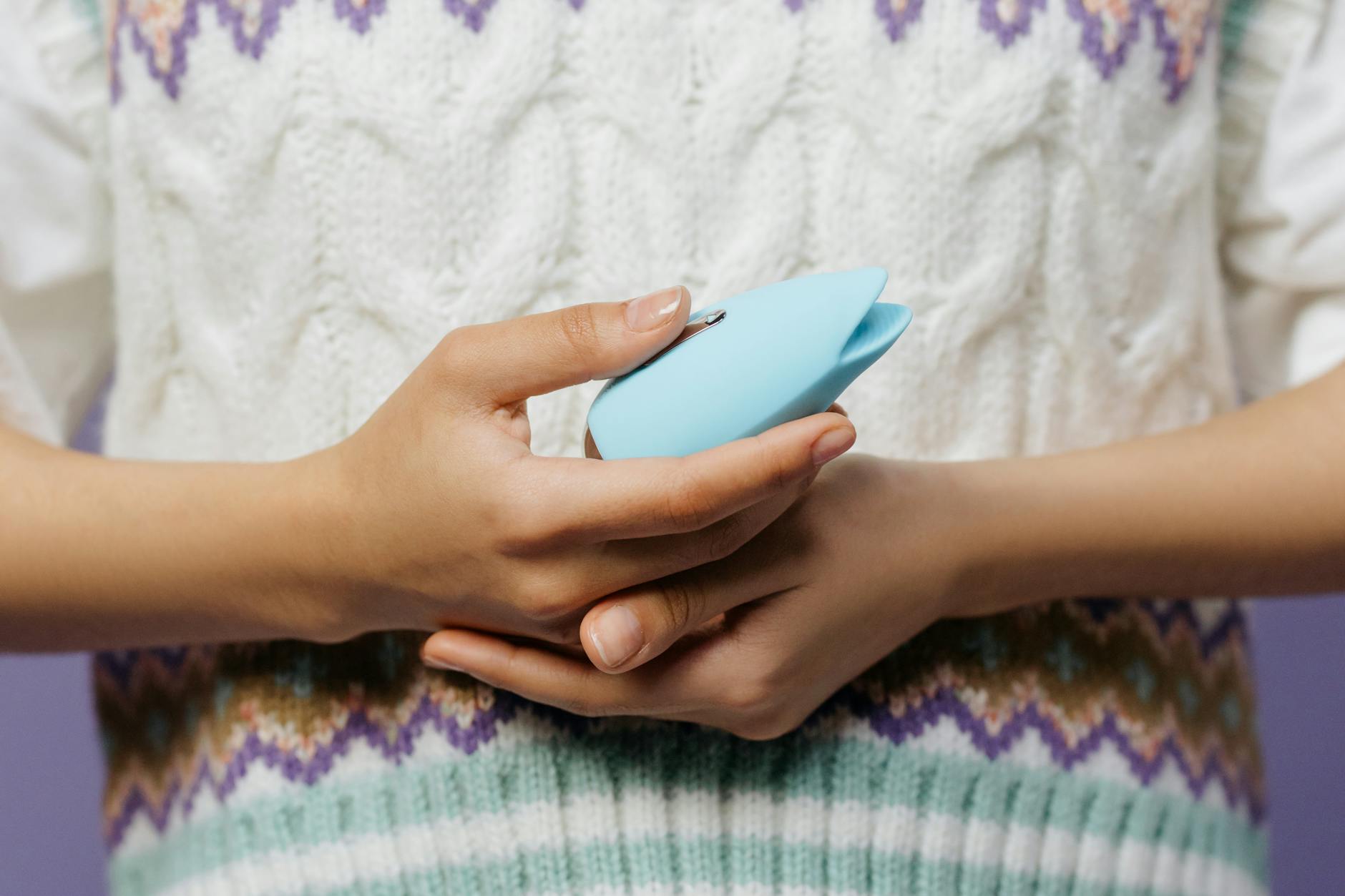 Close-up of hands holding a personal vibrator against a textured surface, showing application method