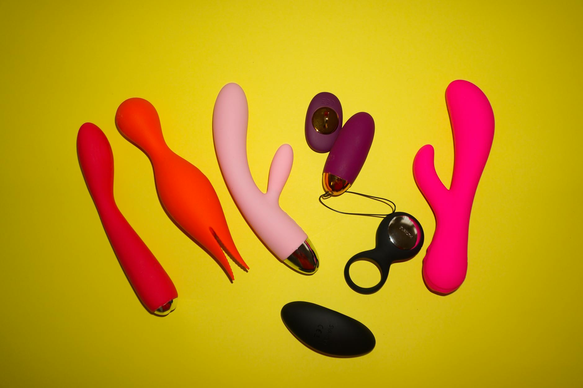 Two hands holding pink and blue lemon clitoral vibrators against a soft pastel background